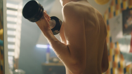 Muscular schoolboy doing dumbbells curls in his room. Closeup of his arms and muscular abs. Weight training, fitness, physical activity. Healthy lifestyle concept. Athlete boy.