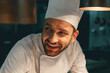 © Friends Stock - Close up of smiling male chef in uniform standing on kitchen of restaurant and looking away