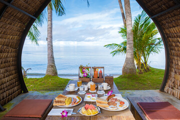 Wall Mural - breakfast table on the beach with palm trees in Thailand. colorful breakfast with eggs and fruit on the Island of Koh Mak