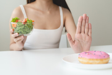 Poster - Woman on dieting for good health concept. Close up female using hand push out her favourite donut and choose green apple and vegetables for good health.