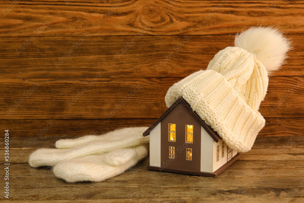 House model with warm hat and mittens on dark wooden background. Heating concept