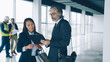 © silverkblack - Asian businesswoman talking to partner studying papers standing indoors in modern glass walls building duscussing real estate deal.
