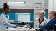 © DC Studio - General practitioner consulting man with physical disability, talking to patient and wife at chekcup visit. Wheelchair user with impairment doing health examination in medical cabinet.