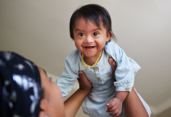 Happy, down syndrome baby and child mom care of a woman holding a kid with a disability at a house. Happiness and smile of a young toddler special needs face from India in a home with a mother