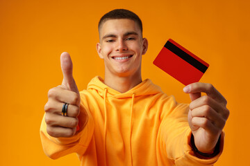 Wall Mural - Handsome young man holding credit card on yellow color background