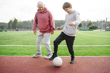 Happy Boy With Grandfather Playing With Soccer Ball At Sports Field