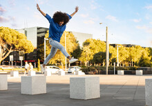 Happy woman with arms raised jumping on concrete block