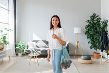 Smiling Woman Carrying Mesh Bag With Vegetables In Living Room