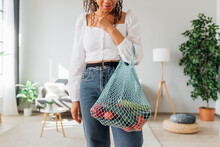 Young Woman Carrying Mesh Bag With Vegetables At Home