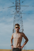Shirtless Young Man With Hands On Hip In Front Of Electric Pylon