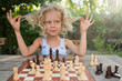 © Westend61 - Cute girl playing with hair sitting in front of chessboard