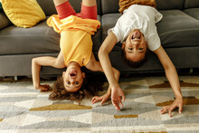 Girl And Boy Sticking Out Tongue Enjoying Upside Down On Sofa At Home