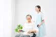 室内で高齢者女性の乗った車椅子を押す介護士
