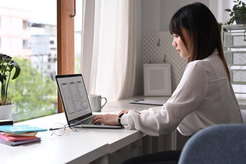 Wall Mural - side view of young asian woman web developer working with prototype wireframe for web mobile phone o