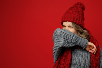 Wall Mural - Young sad sick woman with runny nose wear warm gray sweater scarf hat sneeze into sleeve isolated on plain red background studio portrait Healthy lifestyle ill disease treatment cold season concept