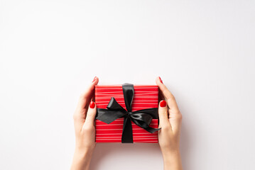 Wall Mural - Black friday sales concept. First person top view photo of woman's hands giving red giftbox with black ribbon bow on isolated white background with empty space