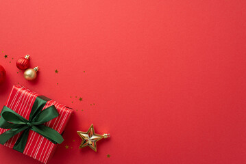 Christmas Day concept. Top view photo of baubles gold star ornament red giftbox with green ribbon bow and confetti on isolated red background with empty space