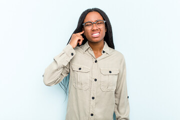 Wall Mural - Young African American woman with braids hair isolated on blue background covering ears with fingers, stressed and desperate by a loudly ambient.