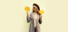 Autumn Portrait Of Beautiful Smiling Young Woman With Yellow Maple Leaves Wearing Round Hat, Coat On White Background
