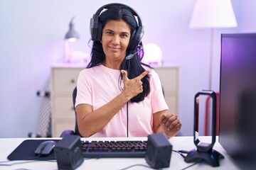 Sticker - Mature hispanic woman playing video games at home cheerful with a smile of face pointing with hand and finger up to the side with happy and natural expression on face