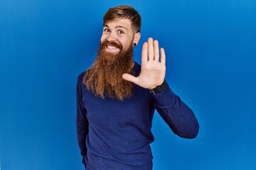 Poster - Redhead man with long beard wearing casual blue sweater over blue background waiving saying hello happy and smiling, friendly welcome gesture