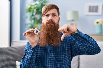 Canvas Print - Caucasian man with long beard holding virtual currency bitcoin with angry face, negative sign showing dislike with thumbs down, rejection concept