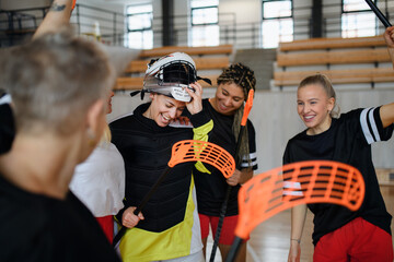 Sticker - Group of young and old cheerful women, floorball team players, in gym cebrating victory.