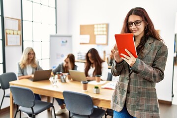 Wall Mural - Young businesswoman smiling happy using touchpad while partners work at the office.