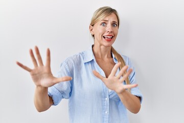 Poster - Beautiful blonde woman standing over white background afraid and terrified with fear expression stop gesture with hands, shouting in shock. panic concept.