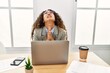 © Krakenimages.com - Beautiful hispanic business woman sitting on desk at office working with laptop begging and praying with hands together with hope expression on face very emotional and worried. begging.