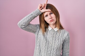 Sticker - Beautiful woman standing over pink background making fun of people with fingers on forehead doing loser gesture mocking and insulting.