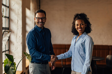 Portrait of two business people, standing and shaking hands, smiling for the camera.