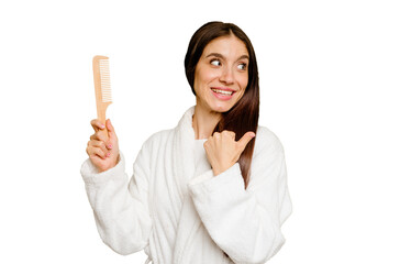 Young caucasian woman holding an hair comb isolated points with thumb finger away, laughing and carefree.