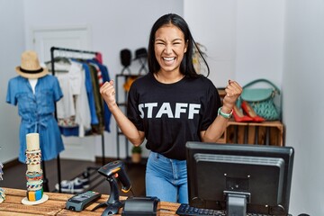 Wall Mural - Young hispanic woman working as staff at retail boutique very happy and excited doing winner gesture with arms raised, smiling and screaming for success. celebration concept.