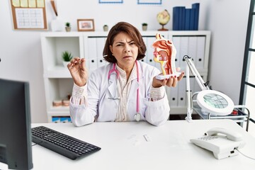 Poster - Middle age hispanic doctor woman holding coronavirus infection nasal test clueless and confused expression. doubt concept.