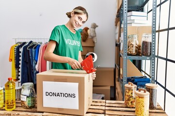 Wall Mural - Young caucasian woman wearing volunteer uniform packing donations box at charity center