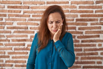 Wall Mural - Brunette woman standing over bricks wall touching mouth with hand with painful expression because of toothache or dental illness on teeth. dentist