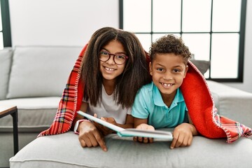 Wall Mural - Two siblings lying on the sofa reading a book with a happy and cool smile on face. lucky person.