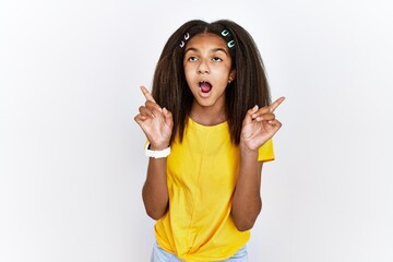 Wall Mural - Young african american girl standing over white isolated background amazed and surprised looking up and pointing with fingers and raised arms.