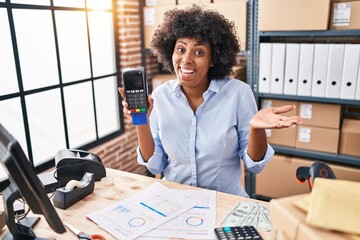 Poster - Black woman with curly hair working at small business ecommerce holding credit card and dataphone celebrating achievement with happy smile and winner expression with raised hand