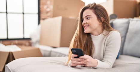 Sticker - Young blonde woman using smartphone lying on sofa at new home