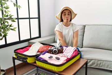 Poster - Beautiful middle age hispanic woman packing summer clothes in suitcase making fish face with lips, crazy and comical gesture. funny expression.