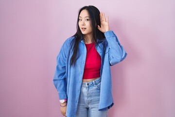 Canvas Print - Young asian woman standing over pink background smiling with hand over ear listening an hearing to rumor or gossip. deafness concept.