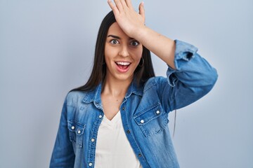 Sticker - Hispanic woman standing over blue background surprised with hand on head for mistake, remember error. forgot, bad memory concept.