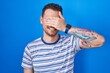 © Krakenimages.com - Young hispanic man standing over blue background smiling and laughing with hand on face covering eyes for surprise. blind concept.