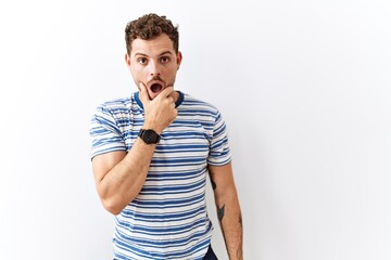 Poster - Handsome young man standing over isolated background looking fascinated with disbelief, surprise and amazed expression with hands on chin