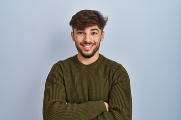 Sticker - Arab man with beard standing over blue background happy face smiling with crossed arms looking at the camera. positive person.