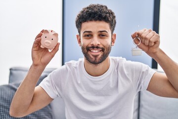 Canvas Print - Arab man holding piggy bank and house keys smiling with a happy and cool smile on face. showing teeth.