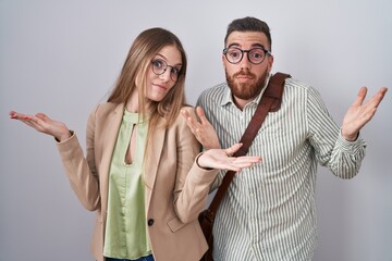 Wall Mural - Young couple standing over white background clueless and confused expression with arms and hands raised. doubt concept.