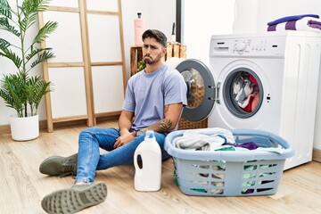 Wall Mural - Young hispanic man putting dirty laundry into washing machine depressed and worry for distress, crying angry and afraid. sad expression.